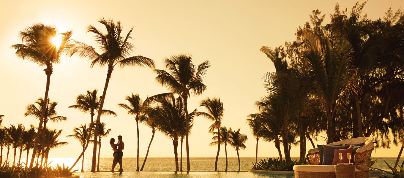 Destination wedding couple next to resort pool and beach at sunset.