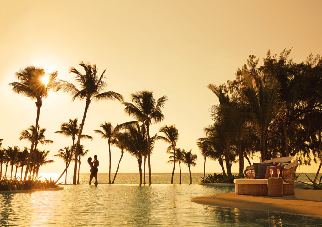 Couple next to pool with a view of a sunset over the ocean during romatic getaway.