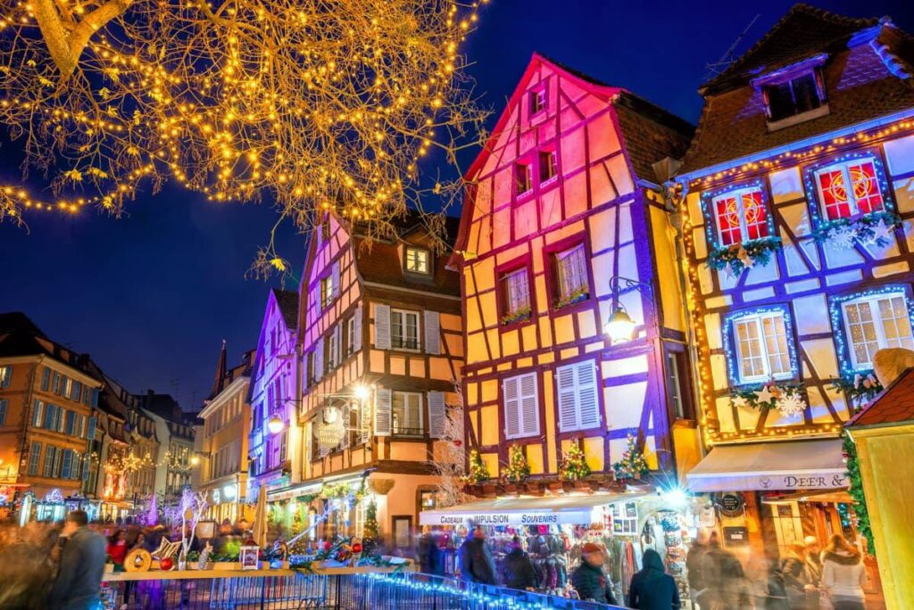 Half-timbered houses of Colmar in Alsace lit up above festive Christmas market stalls at night